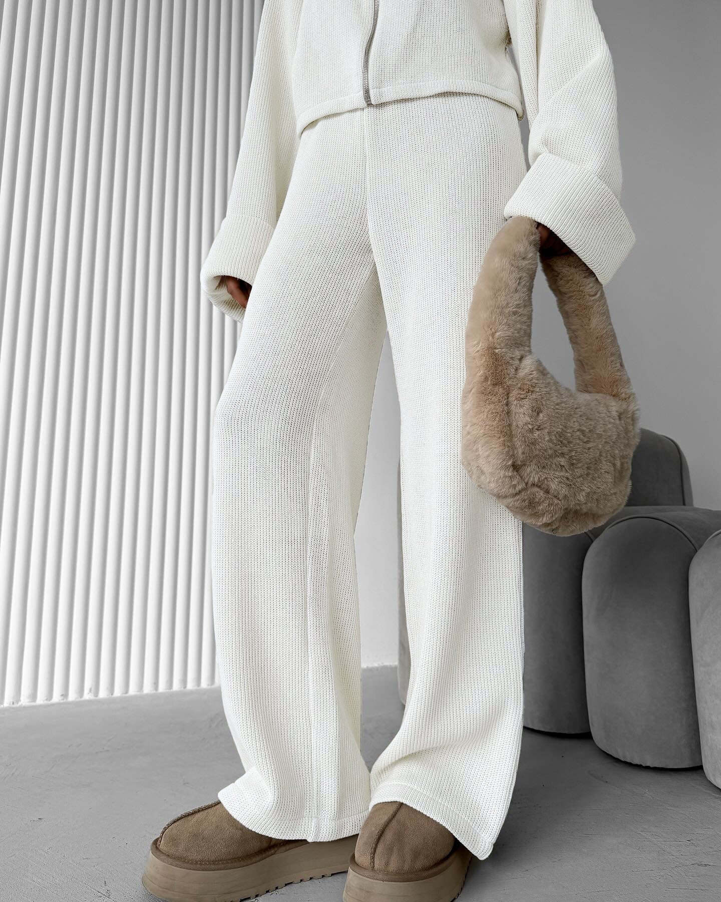 Close view of person wearing a white knit lounge set with a fluffy brown handbag in a minimalistic setting.