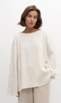 Woman wearing a white knit sweater and beige pants against a plain background