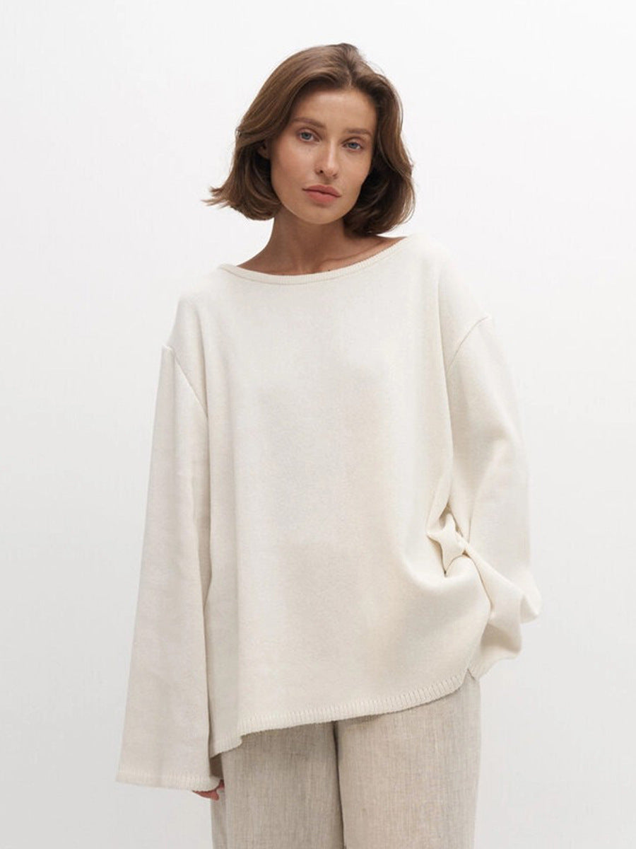 Woman wearing a white knit sweater and beige pants against a plain background