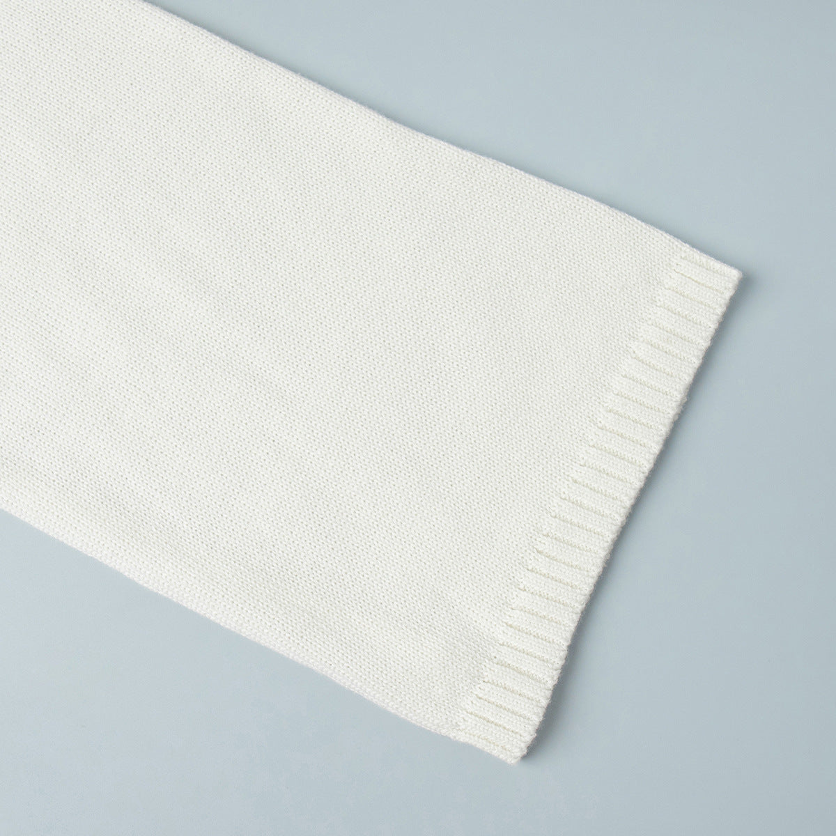Sleeve cuff detail of white knit sweater with ribbed knit edge