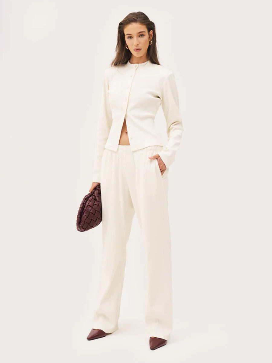 Woman wearing a white co ord set holding a brown handbag on a light gray background