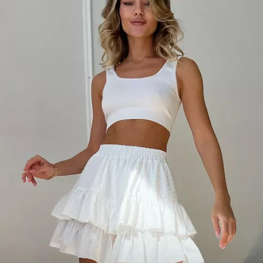 Woman smiling while wearing a white ribbed crop top and a white ruffled polka dot mini skort, standing against a white wall.