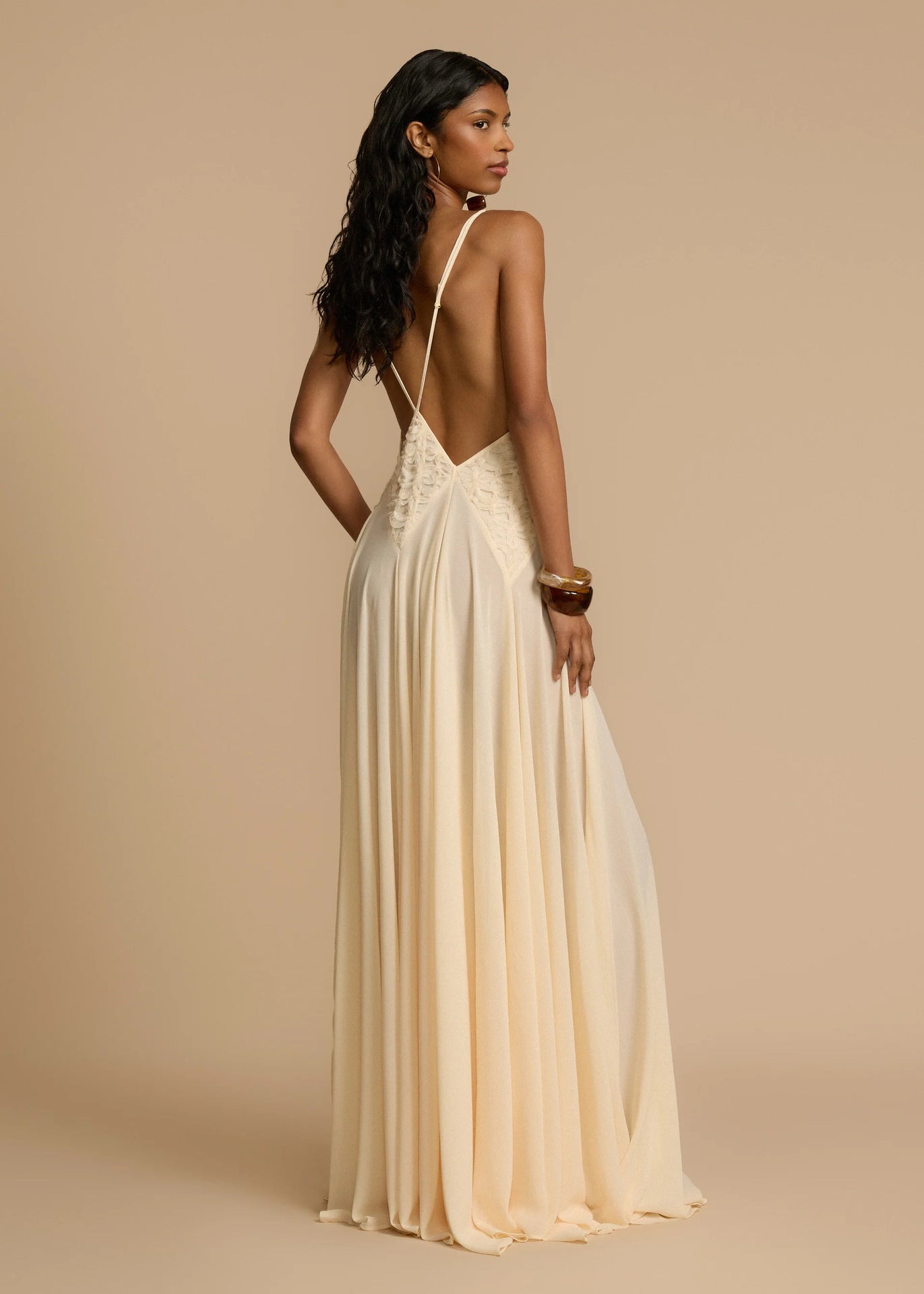 Woman wearing a white deep V vacation maxi dress with lace waist and flowing hem against a beige background