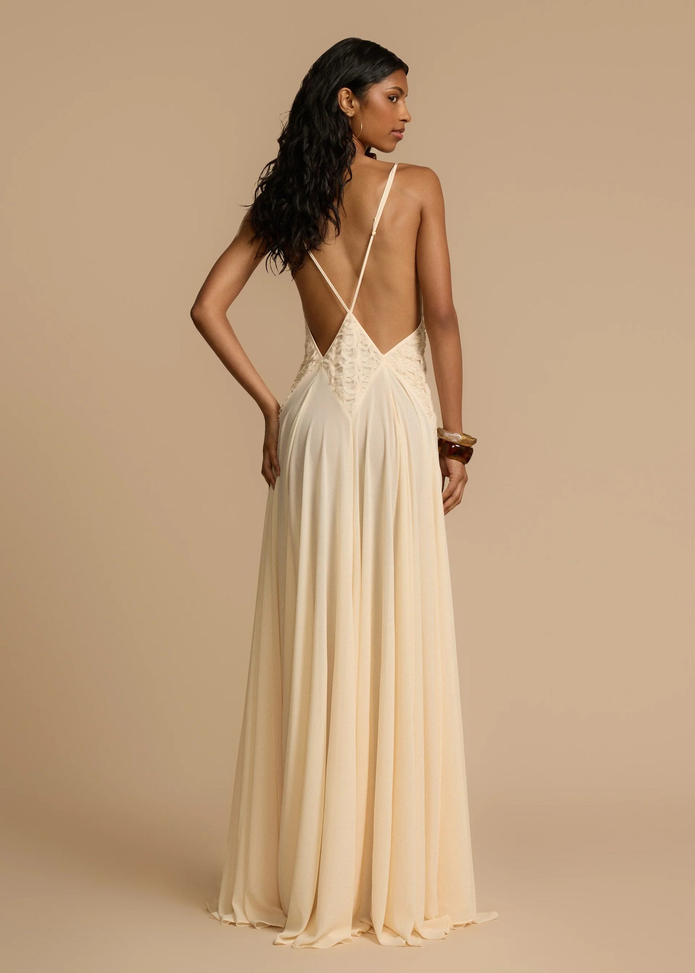 Back view of woman wearing a white v-neck maxi dress with a open back on a beige background