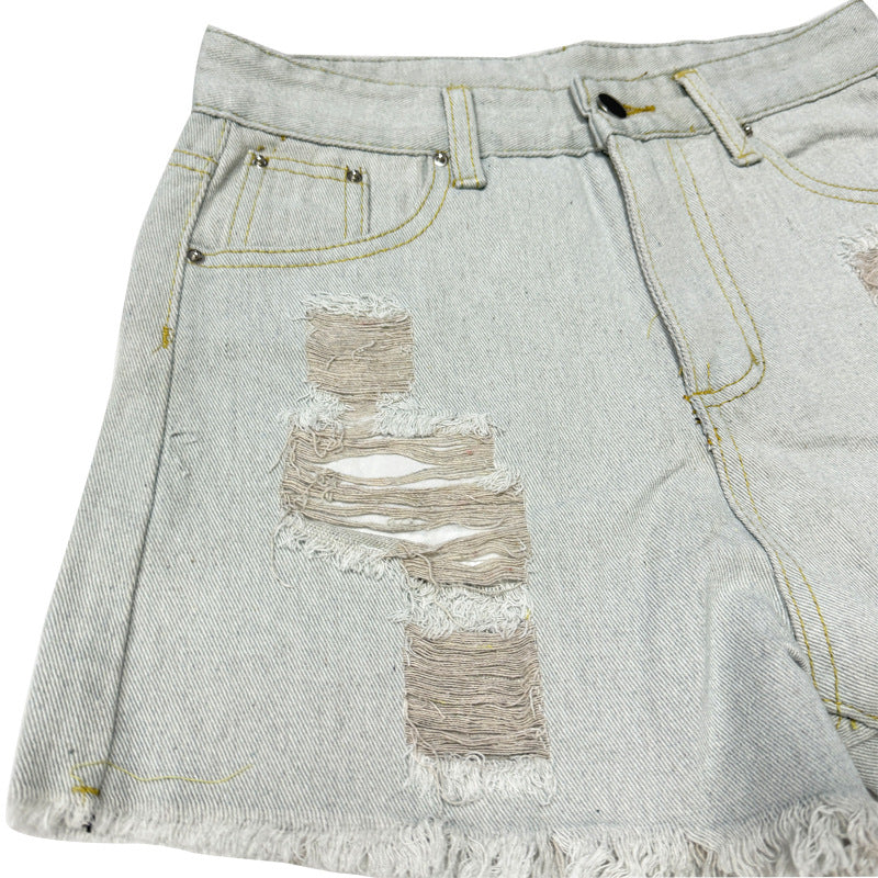 Close-up of distressed detailing on light wash denim shorts showing frayed fabric and stitching.