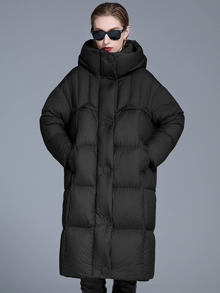 A woman wearing a black quilted oversized puffer coat with wide hood, black sunglasses and red lipstick, posing against gray background