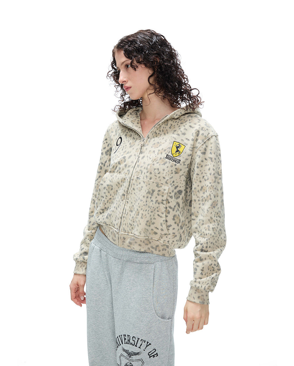 Three-quarter angle shot of a model in a leopard print cropped zip-up hoodie and grey sweatpants.