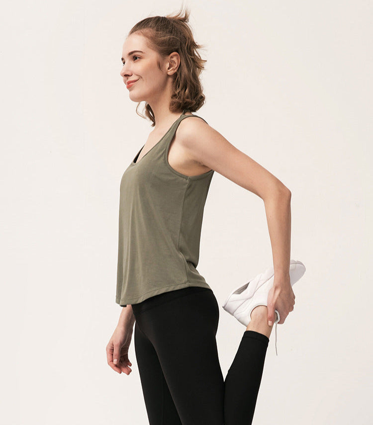 Woman stretching her leg while wearing an amry green tank top and black leggings.