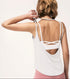 Back view of a woman wearing a white open-back tank top over a criss-cross sports bra.