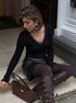 Model seated on steps wearing black V-neck pearl-trim knit top, long sleeves, slim fit, with mini skirt and knee boots.