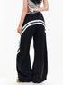 Back view of female model in black wide leg track pants with curved contrast stripes across the rear.