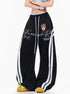 Female model wearing black vintage baggy sweatpants with white side stripes and graphic crest print.