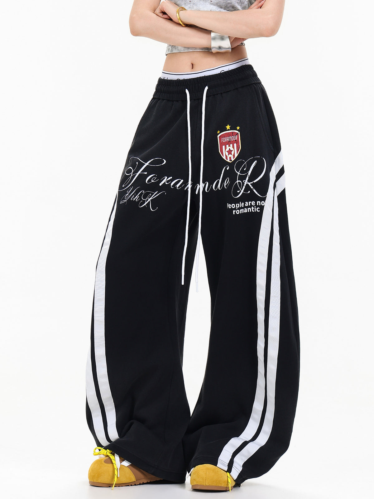 Female model wearing black vintage baggy sweatpants with white side stripes and graphic crest print.
