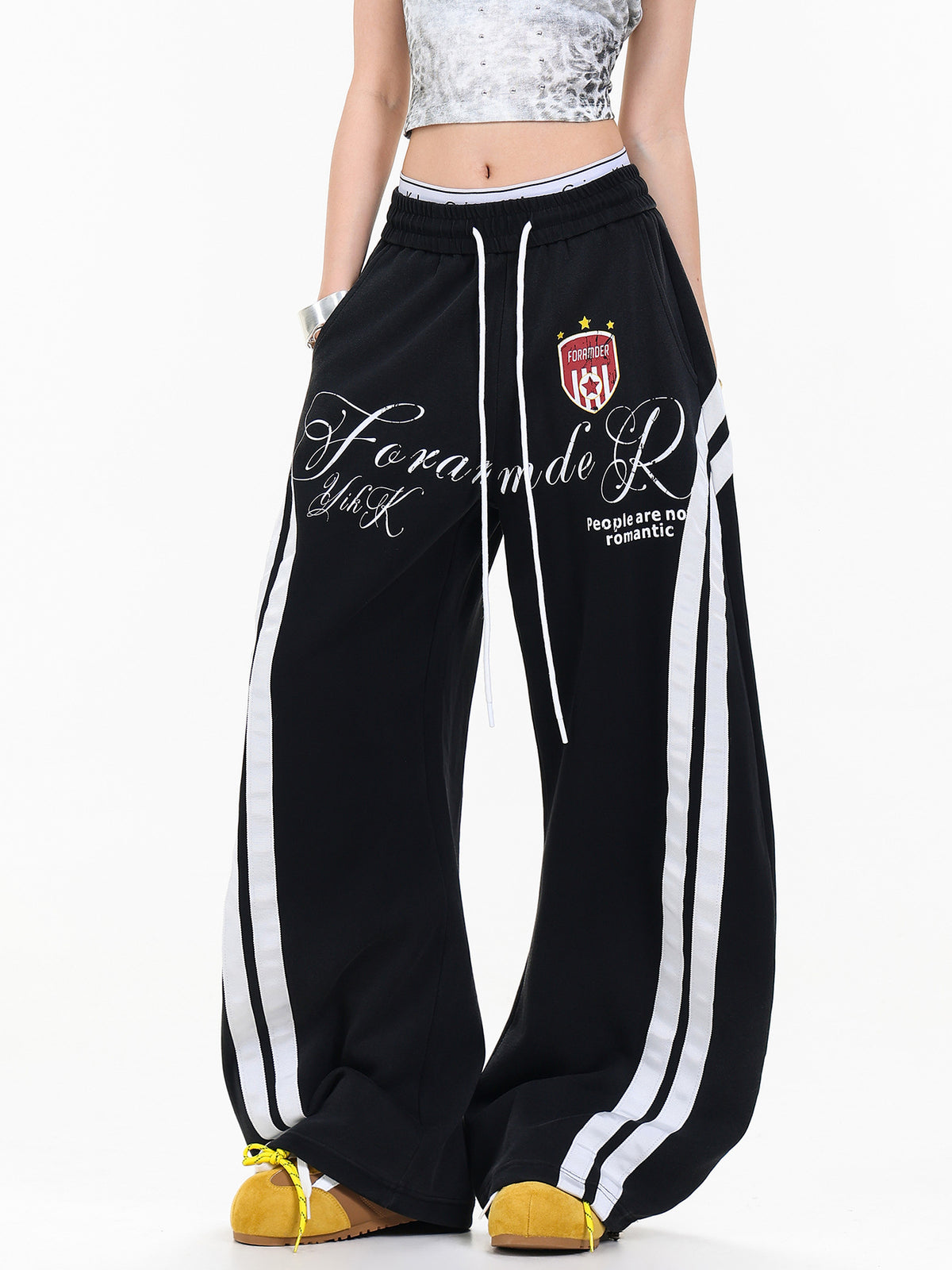 Full length front view of black graphic print wide leg sweatpants paired with crop top and sneakers.