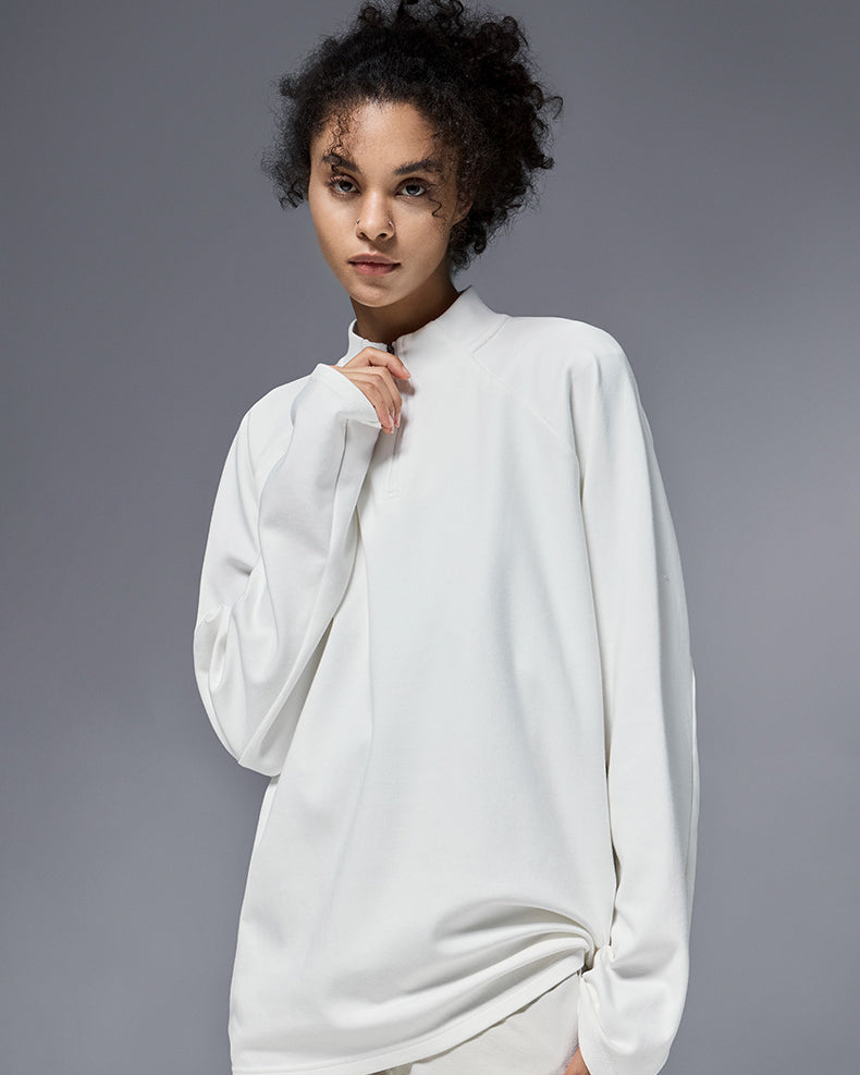 Woman wearing white half zip long sleeve t shirt against a gray background