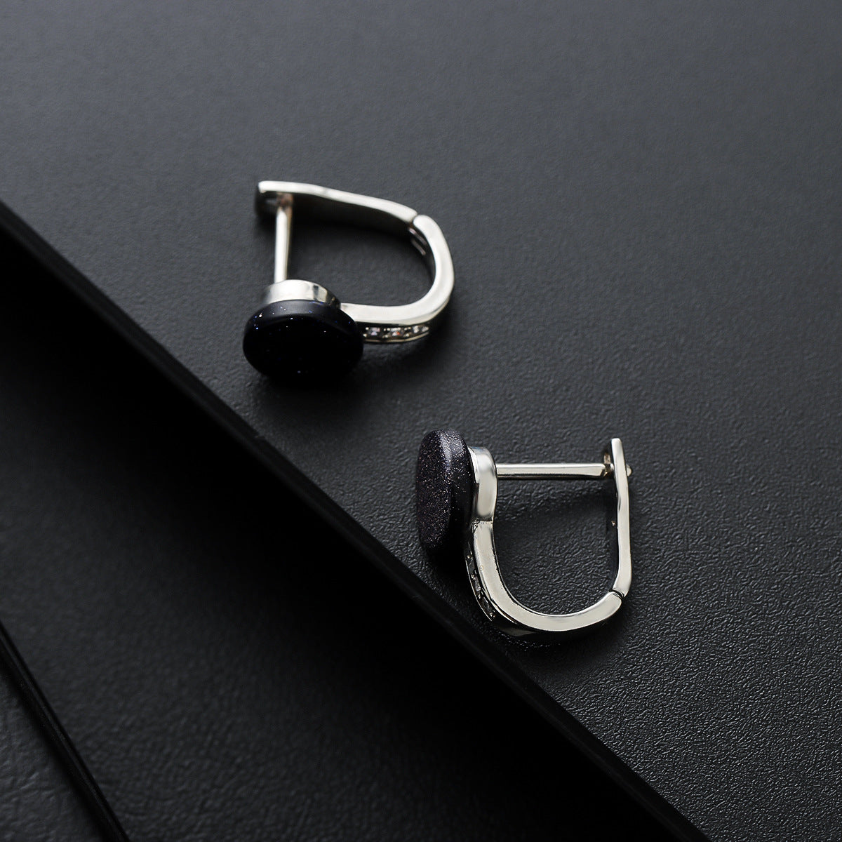 Pair of silver stud earrings with round black stone on dark surface.