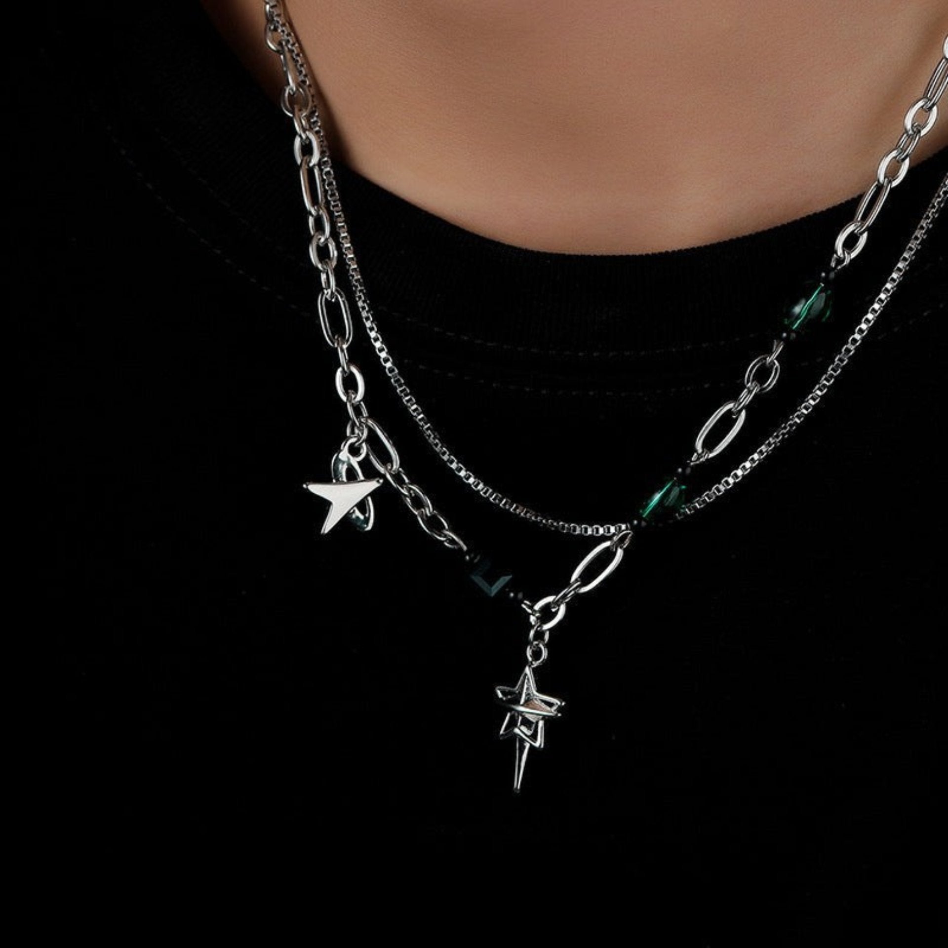 Person wearing layered silver chains with star and arrowhead charms.