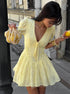 Woman in a yellow dress holding a lemon and a string bag on a city street.