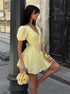 Woman in a yellow dress standing against a textured wall.