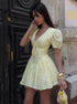Woman in a yellow dress standing against a textured wall.